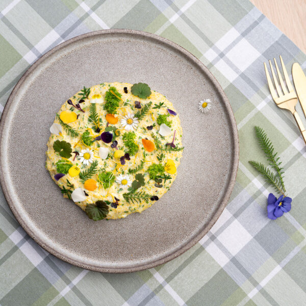 Bunter Frühlingskräuterpolenta auf grauem Teller auf einer karrierten Tischdecke.