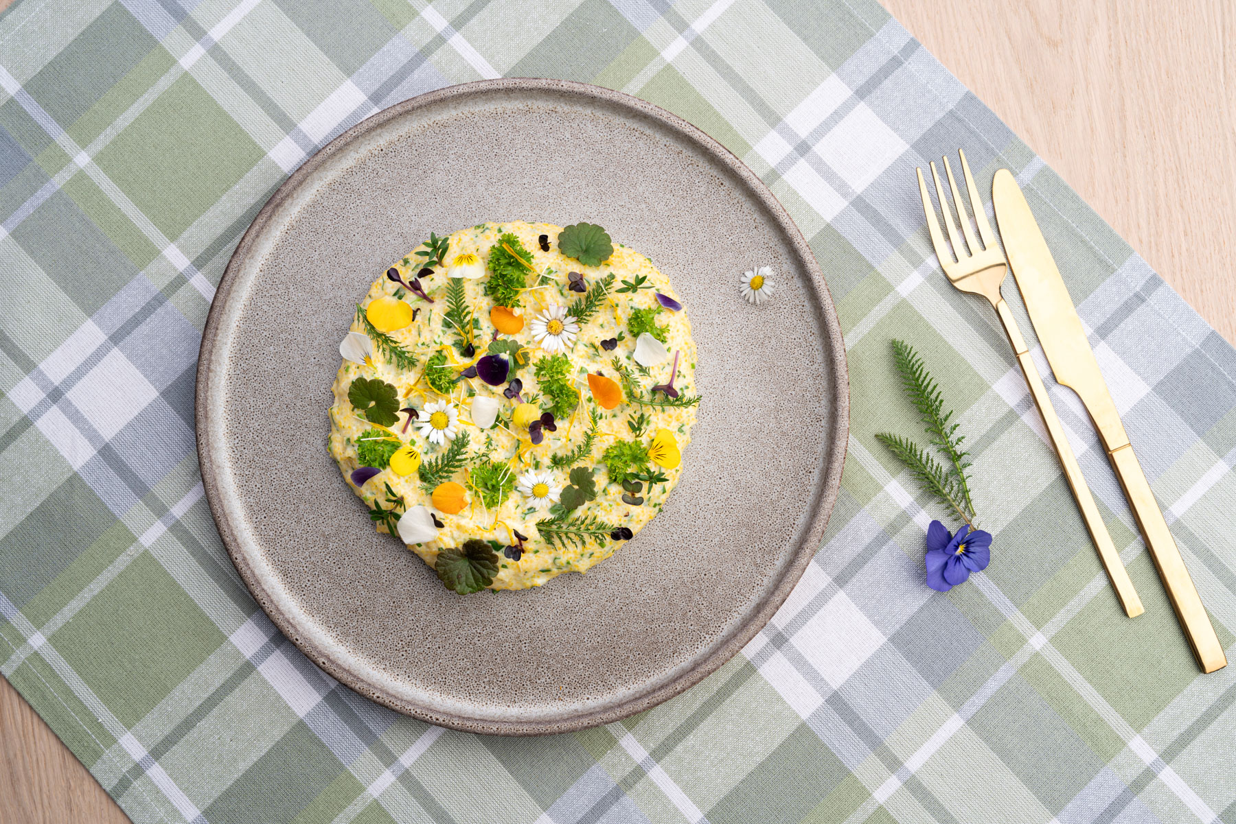 Bunter Frühlingskräuterpolenta auf grauem Teller auf einer karrierten Tischdecke.