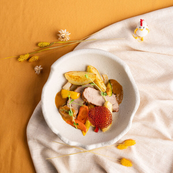 Gebratenes Kalbskarree mit Beilagen in weißer Schüssel auf weißer Tischdecke