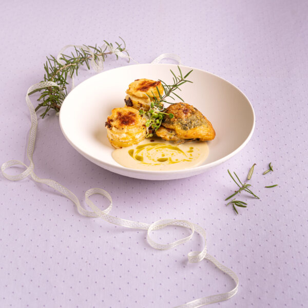 Gefülltes Kräuterhändl mit Erdäpfelgratin in weißem Teller vor lila Hintergrund