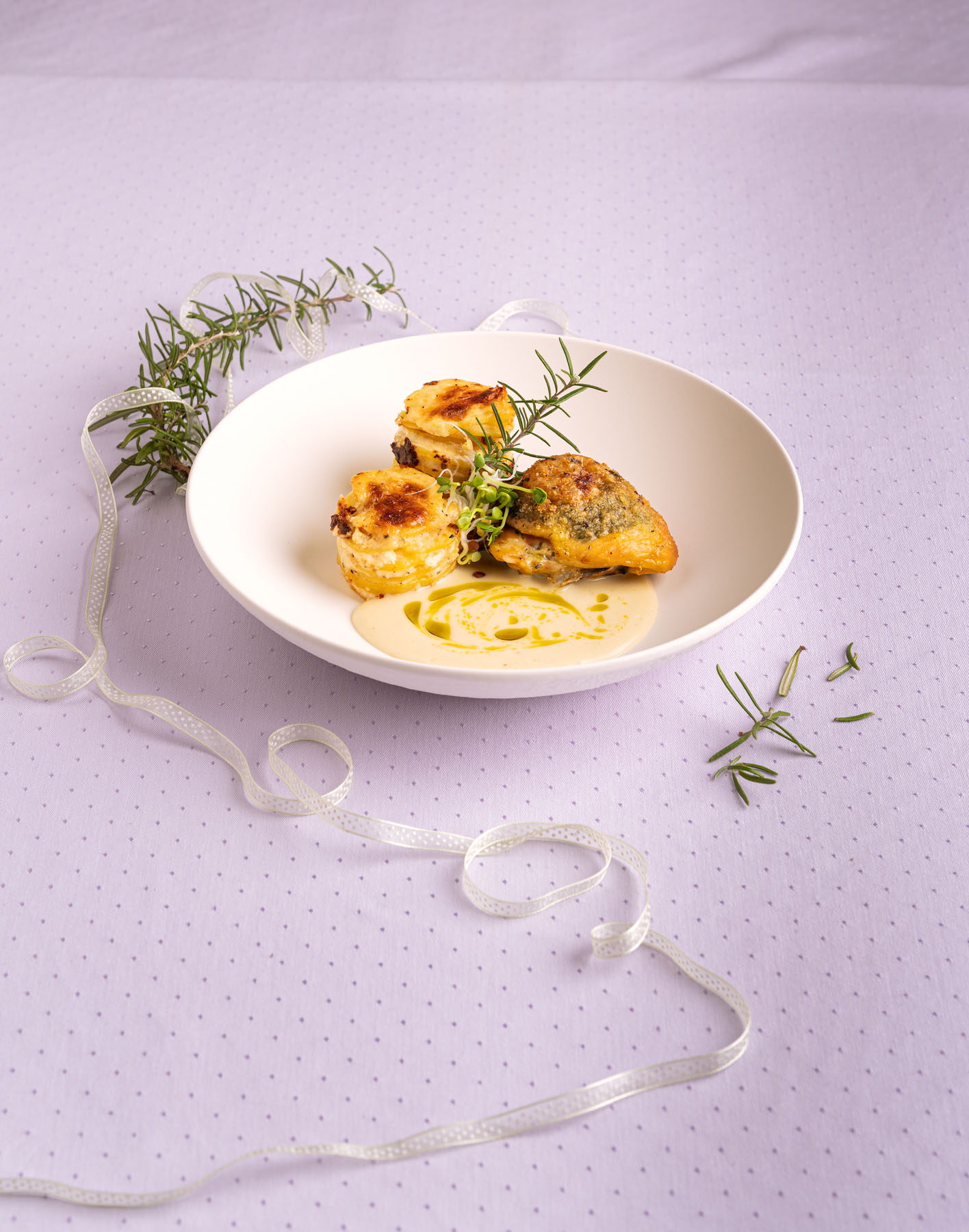 Gefülltes Kräuterhändl mit Erdäpfelgratin in weißem Teller vor lila Hintergrund