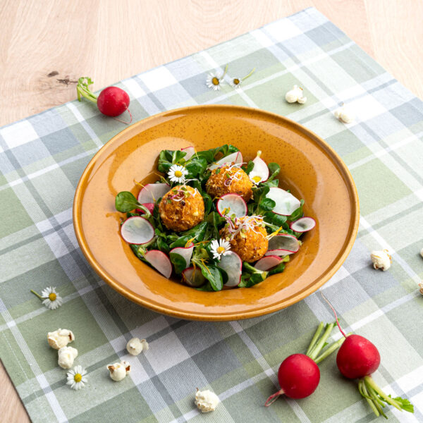 Bunter Frühlingssalat mit Popcornmais auf karrierter Tischdecke in braunem Teller