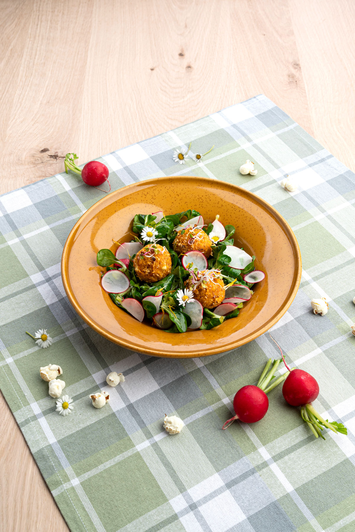 Bunter Frühlingssalat mit Popcornmais auf karrierter Tischdecke in braunem Teller