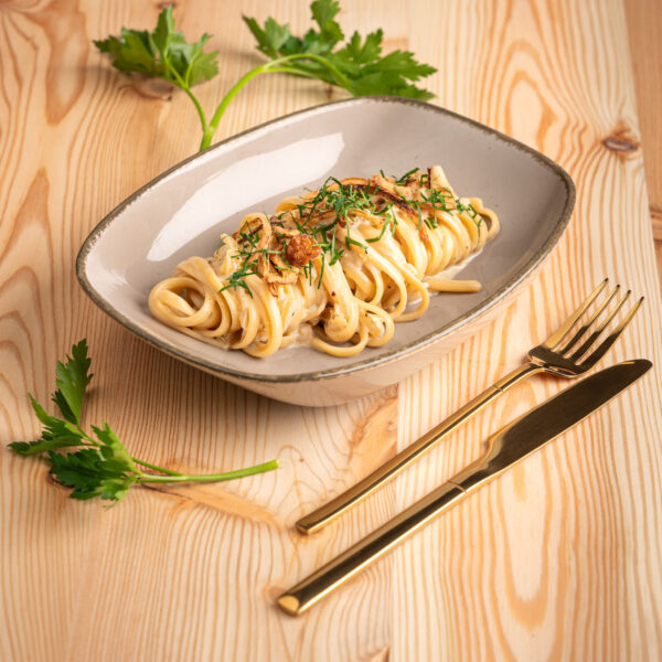 Zwiebelpasta dekoartiv in grauem Teller vor Holzhintergrund